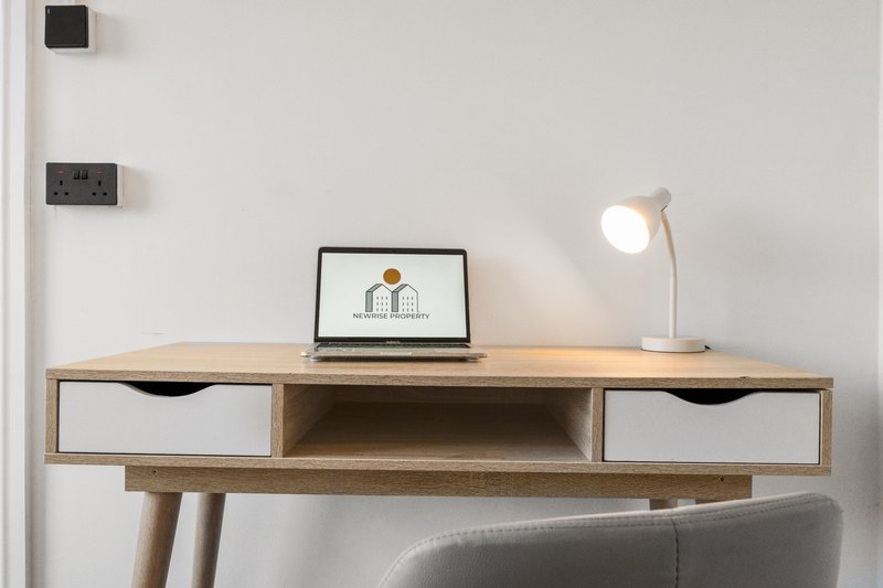 Wooden desk with laptop, white desk lamp, and storage drawers against white wall