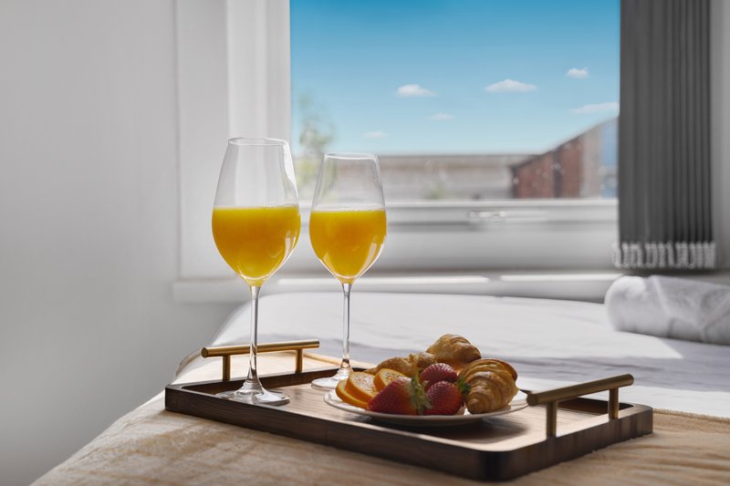 Two glasses of orange juice and fresh pastries on wooden tray by window with city view