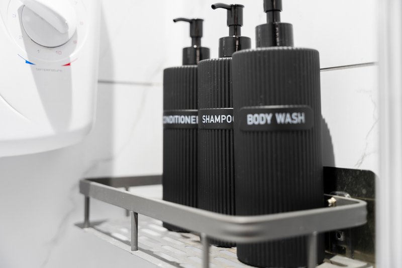 Bathroom shelf with black pump bottles labeled conditioner, shampoo, and body wash