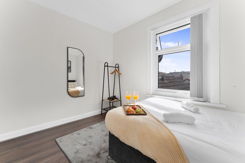 Bright bedroom with double bed, wall mirror, small table with fruit and drinks by window