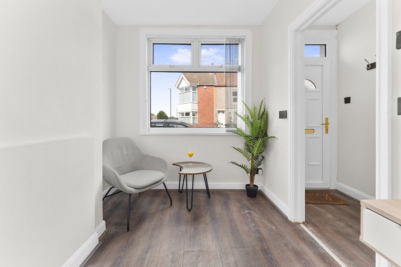 Bright modern hallway with grey armchair, small side table, potted plant and window overlooking street