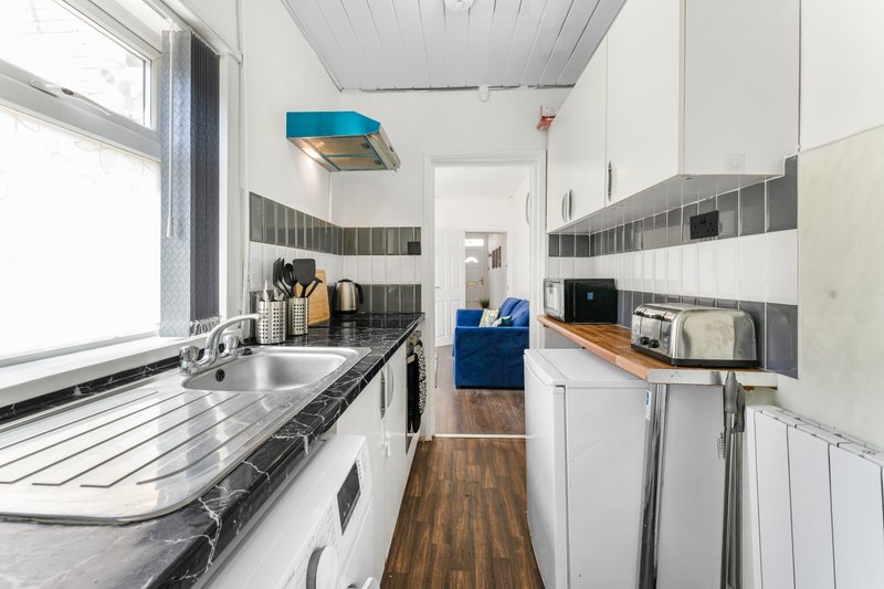 Galley kitchen with white cabinets, black and white tile splashback, wooden worktops and flooring