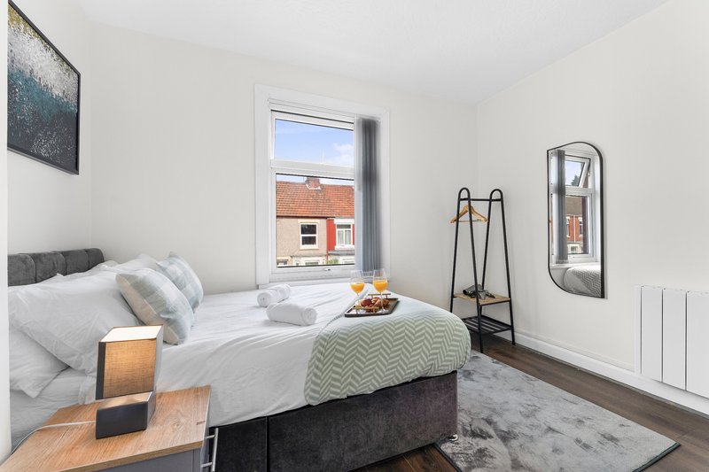 Bright bedroom with double bed, white bedding, wooden floor and brick building view through window