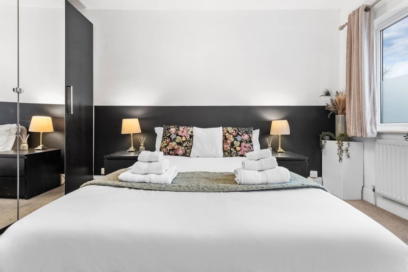 Modern bedroom with black headboard, white bedding, floral cushions, and bedside lamps