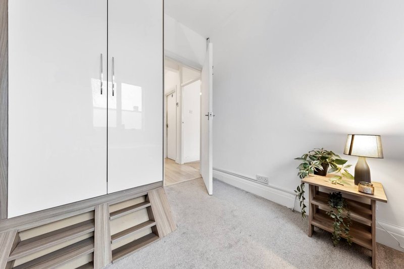 Bright bedroom with wardrobe, wooden dresser, table lamp and open doorway