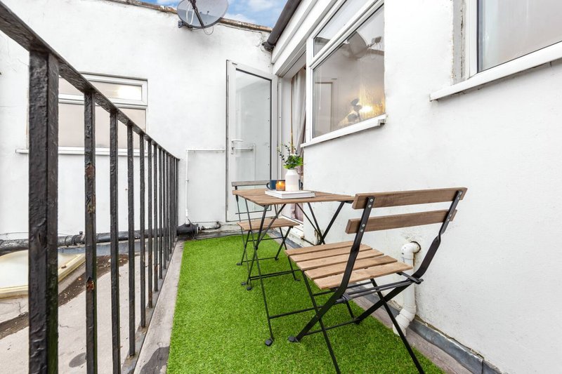 Narrow outdoor patio with artificial grass, wooden table, chairs and black railing