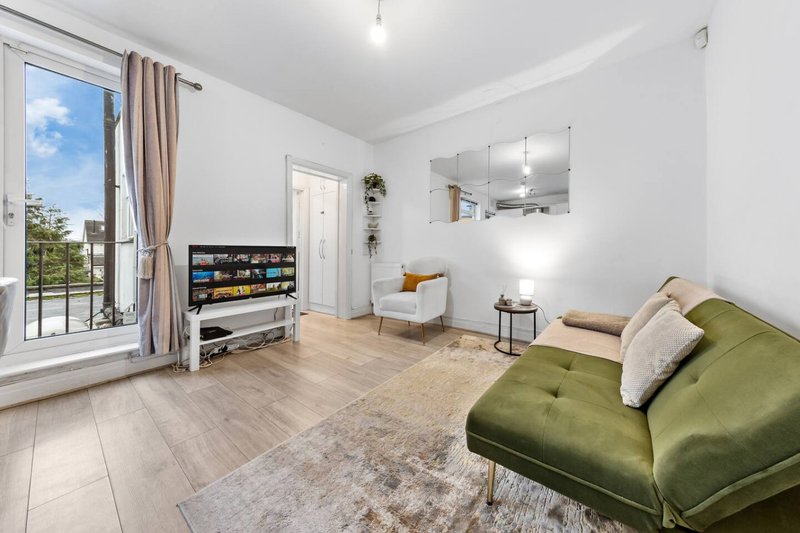 Bright living room with green sofa, TV unit, wooden flooring and balcony access