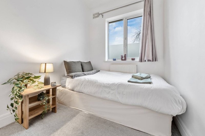 Bright bedroom with single bed, wooden nightstand, lamp, potted plant and window view