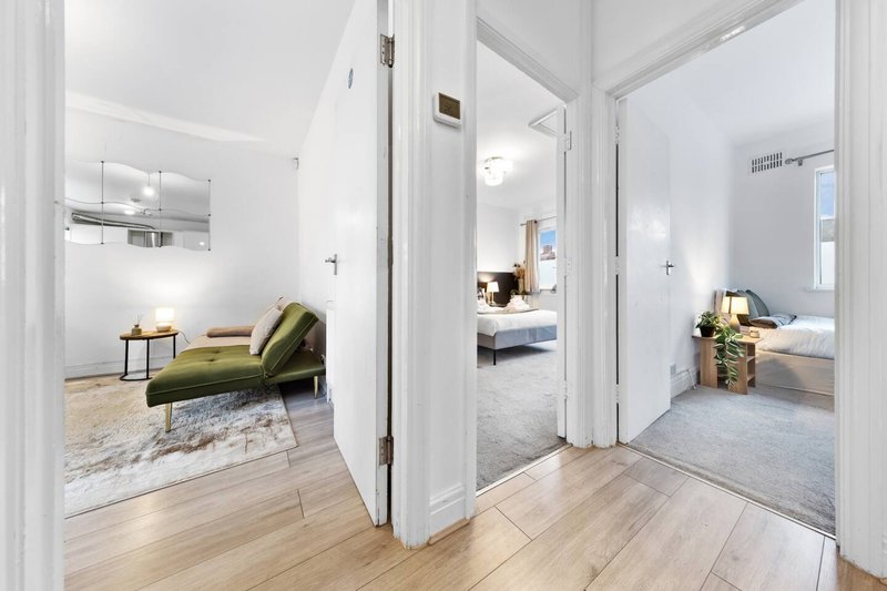 Modern hallway with wood flooring, white walls, green chaise lounge and open doorways to bedrooms
