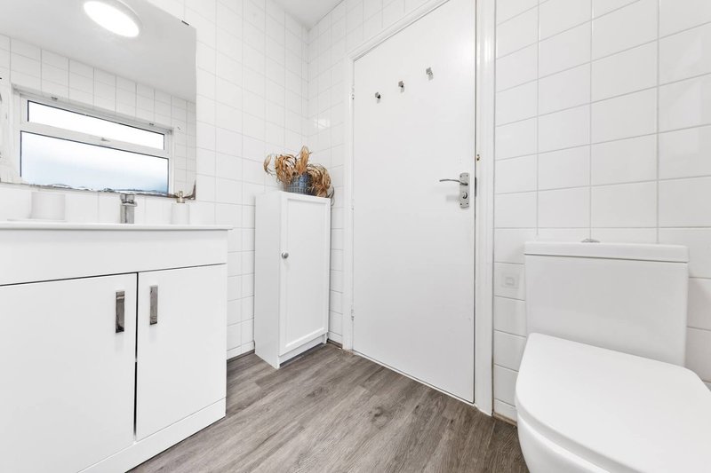 Modern bathroom with white tile walls, vanity sink, toilet, shower enclosure and wooden floor