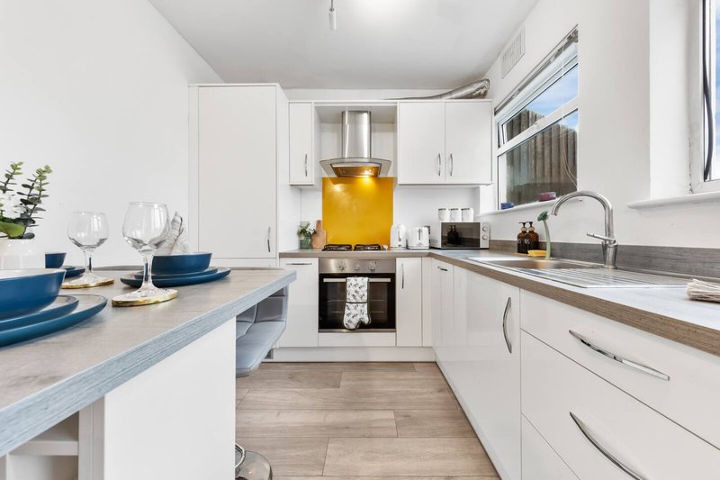 Modern white kitchen with blue tableware, wooden flooring and bright yellow decor