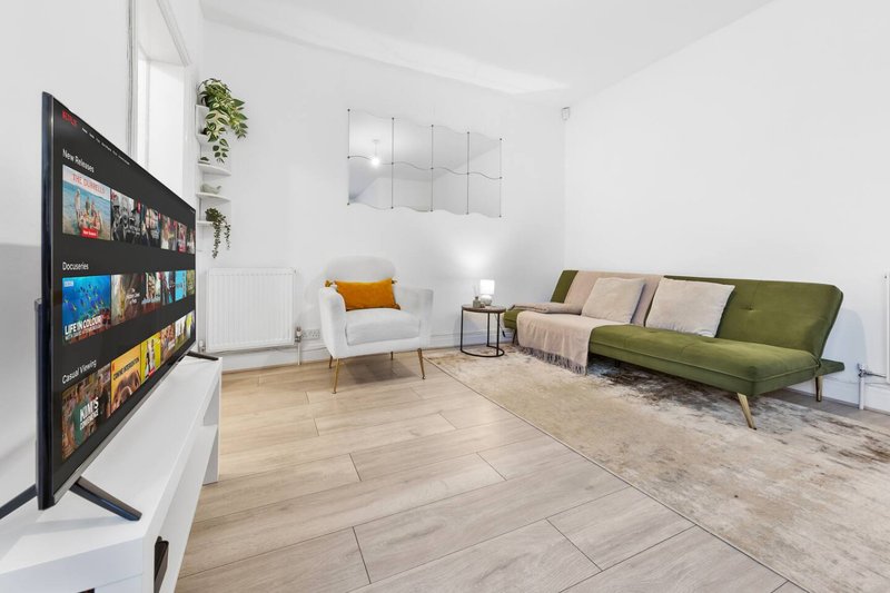 Bright modern living room with TV, white armchair, green sofa and wooden flooring