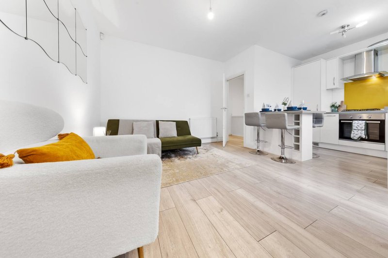 Open-plan living space with white sofas, wooden flooring, kitchen area and yellow accent decor