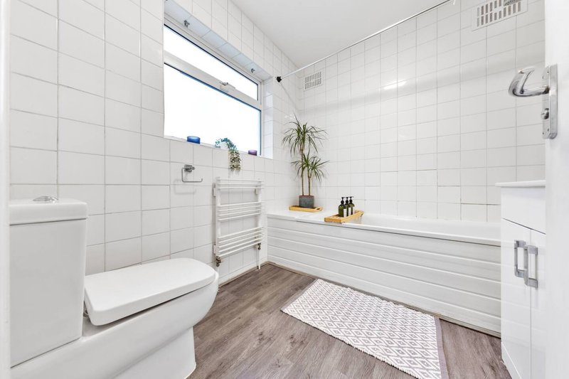 Modern bathroom with white tiles, wooden floor, toilet, bathtub and window