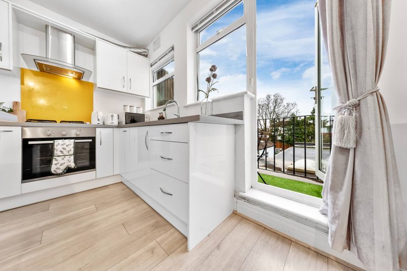 Modern kitchen with white cabinets, yellow range hood, and view to balcony with garden