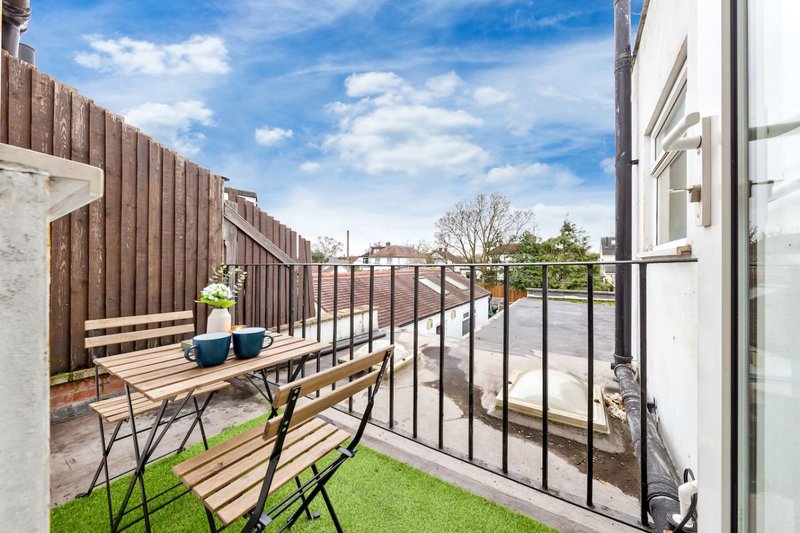 Rooftop terrace with wooden seating, black metal railing and blue sky view