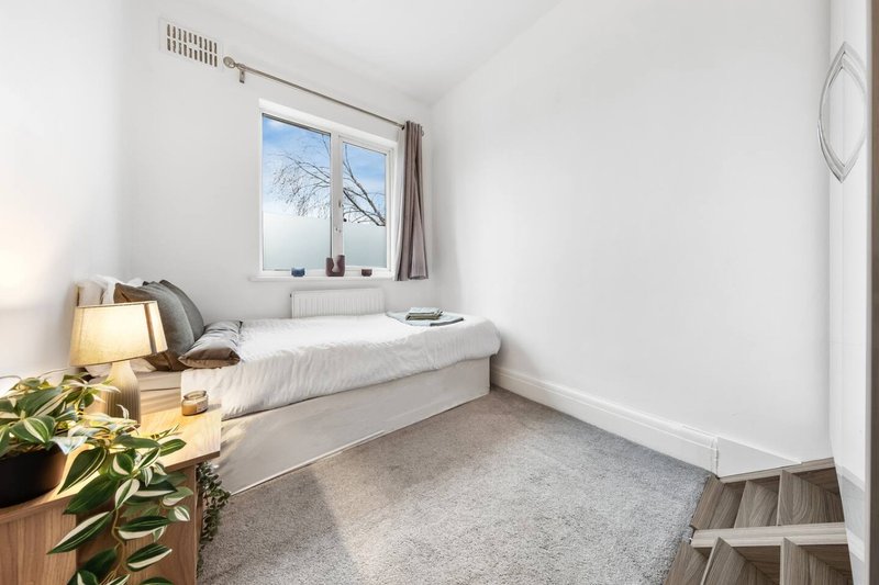Compact bedroom with single bed, wooden nightstand, window view and grey carpet flooring