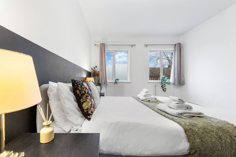 Modern bedroom with double bed, dark headboard, bedside lamp, and windows with countryside views