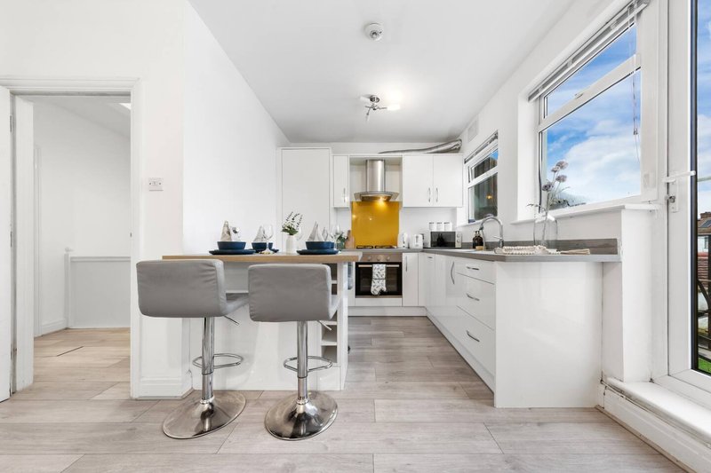 Modern open-plan kitchen with white cabinetry, island with grey bar stools, and large window overlooking garden