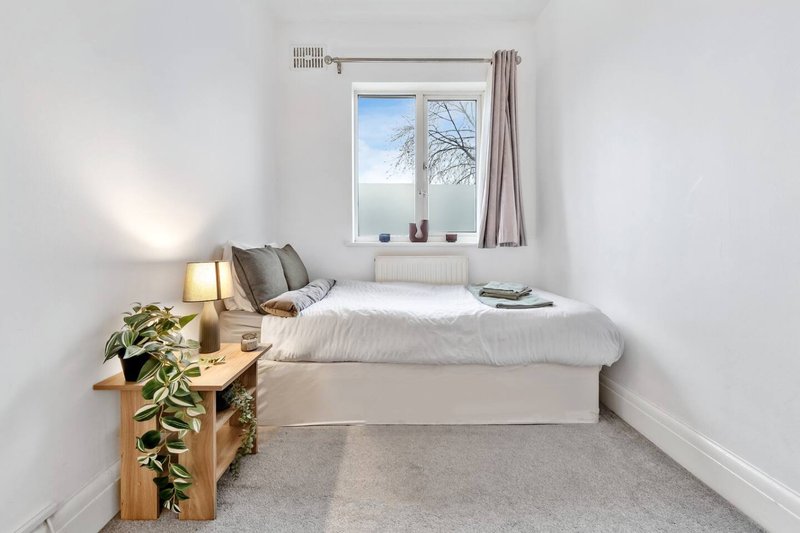 Bright bedroom with single bed, wooden bedside table, potted plant and window with curtains