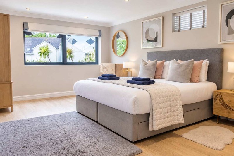 Spacious master bedroom with grey upholstered bed, white bedding, wall art, and large windows