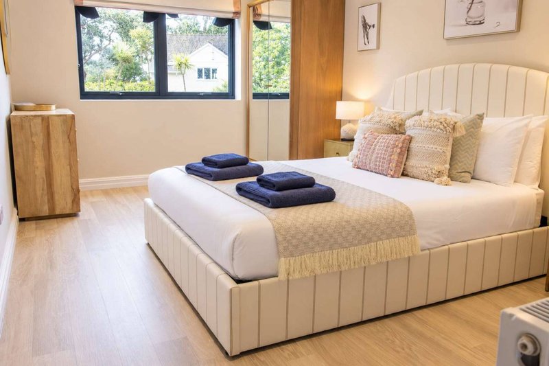 Bright modern bedroom with cream upholstered bed, navy towels, wooden flooring and large windows
