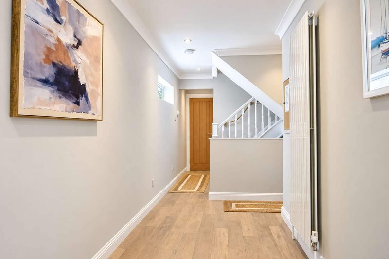 Bright hallway with wooden flooring, white walls, framed artwork and staircase