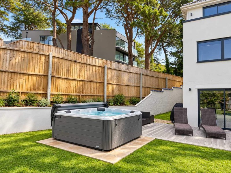 Modern backyard with hot tub, wooden fence, lawn, and contemporary house with large windows