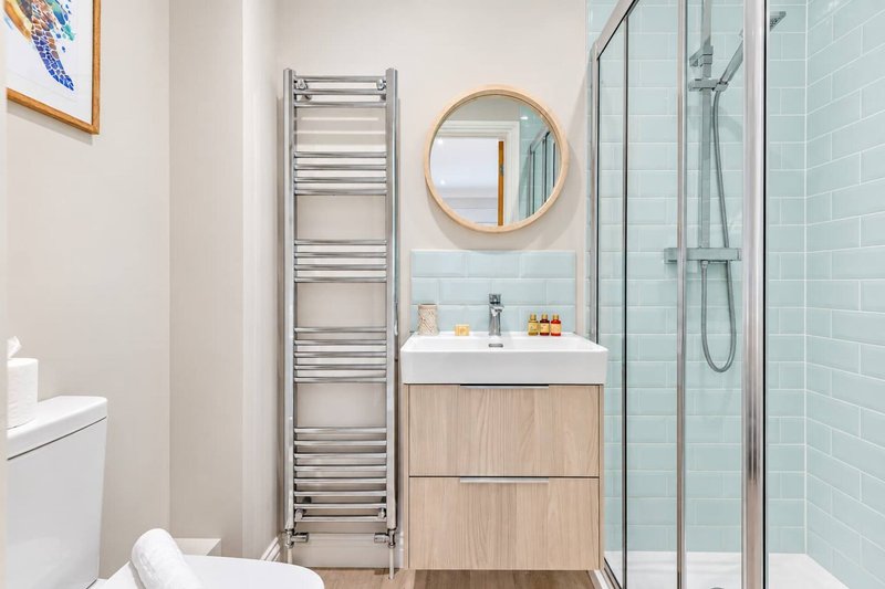 Modern bathroom with vanity, round mirror, towel radiator and walk-in shower