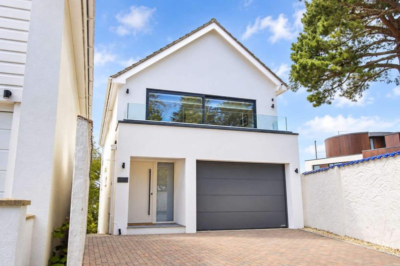 Modern white two-storey house with dark garage door and brick driveway