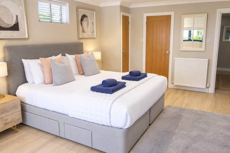 Modern bedroom with grey upholstered bed, white bedding, decorative pillows and folded towels