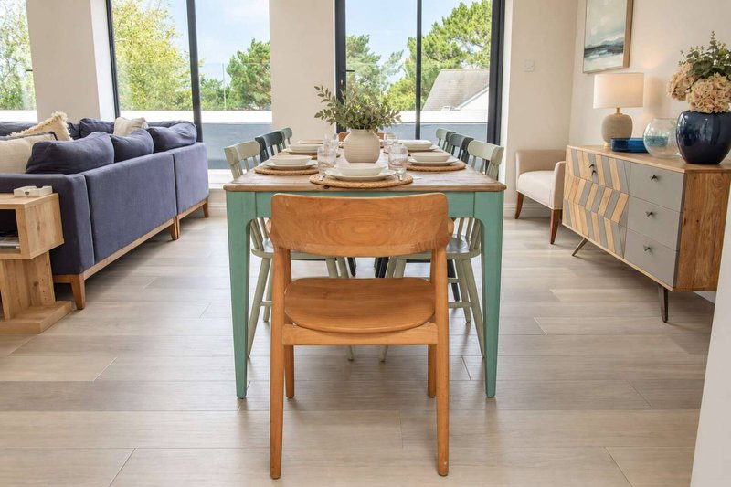 Open-plan living and dining area with wooden dining table, chairs, sofa, and large windows overlooking gardens