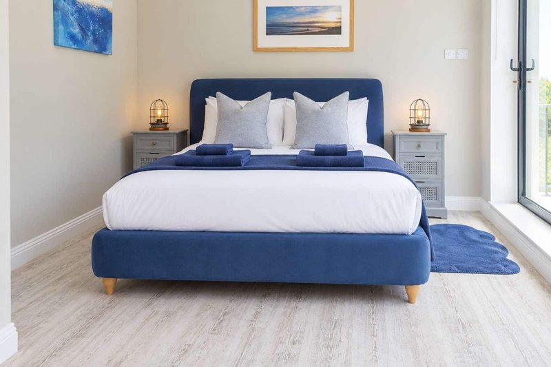 Modern bedroom with navy upholstered bed, white bedding, wooden floor and framed wall art