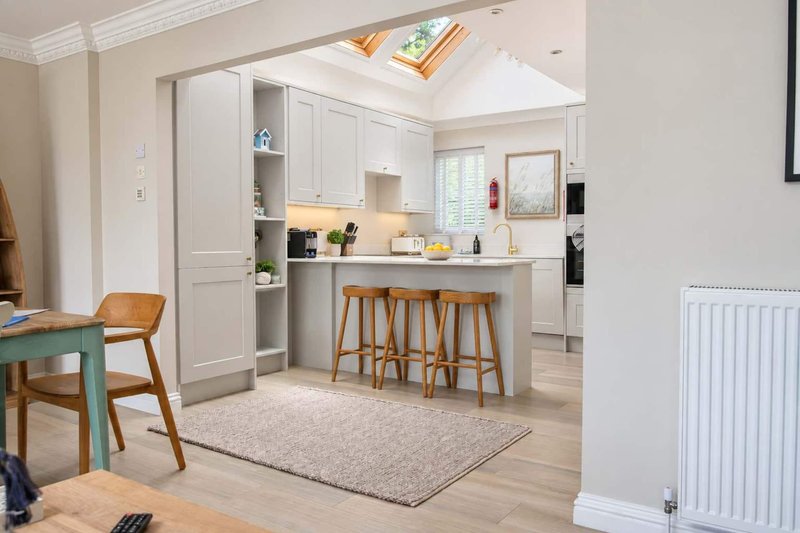 Open-plan kitchen and dining area with white cabinetry, island seating, wooden chairs and skylight