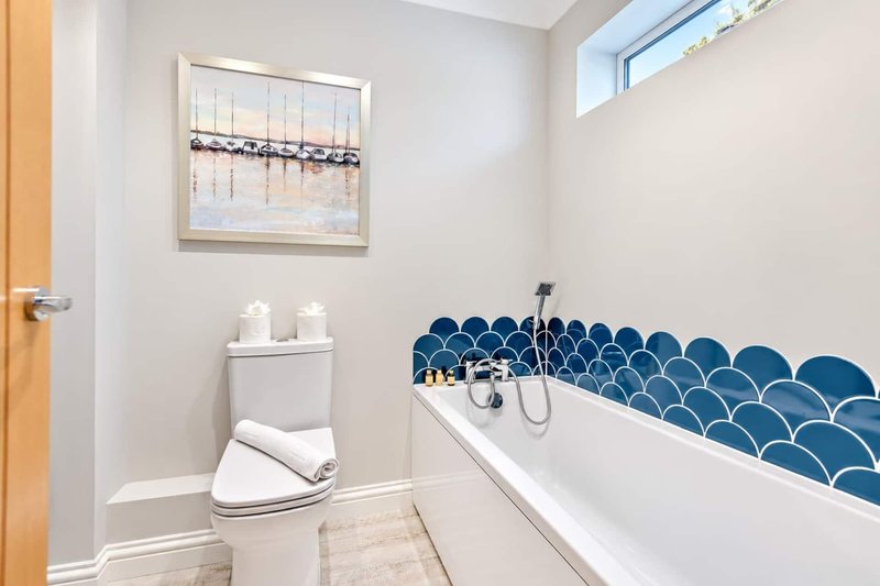 Clean bathroom with white toilet, bathtub with blue tile surround and decorative wall art