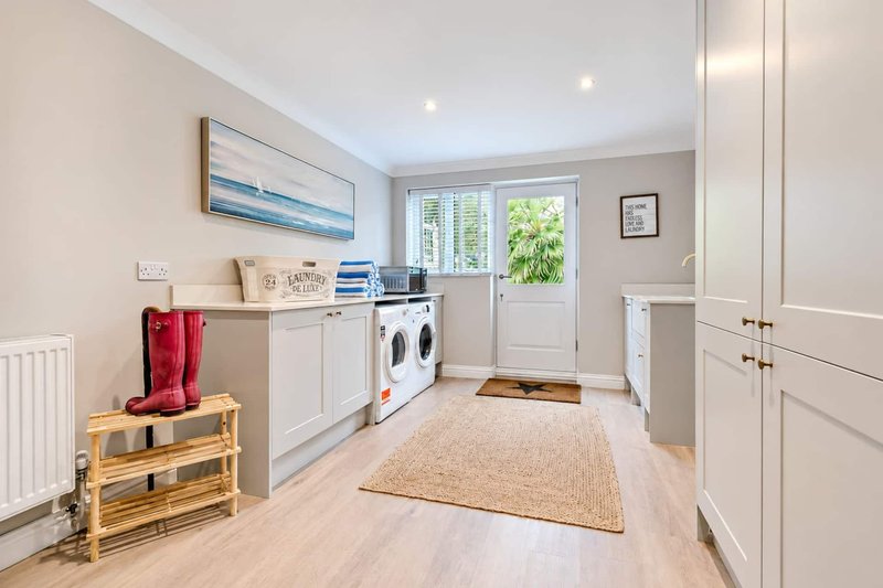 Modern utility room with washing machines, white cabinetry, wooden shelving and door to garden