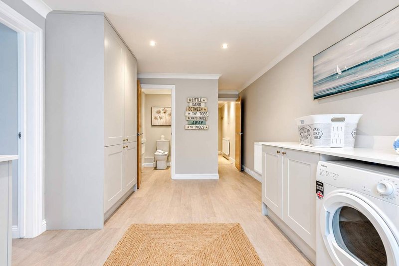 Modern utility room with washing machine, white cabinetry, wooden flooring and doorways to bathroom and hall