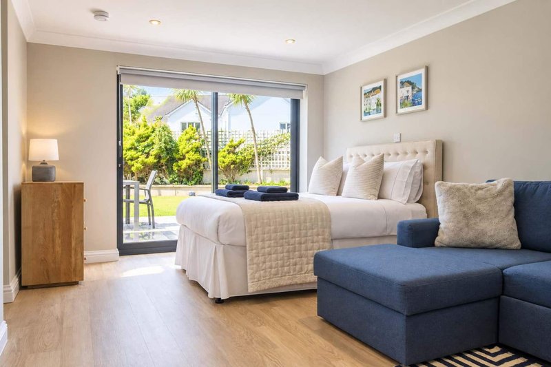 Bright bedroom with double bed, blue sofa, wooden floor and garden view doors