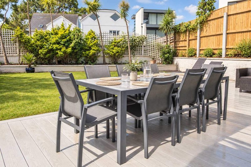 Modern garden patio with dining table, chairs, lawn, fencing and neighbouring houses visible