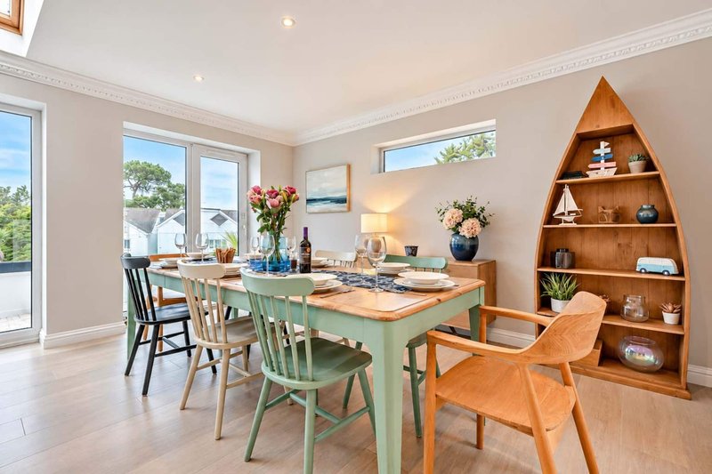 Bright dining room with green table, mixed wood chairs, shelving unit and garden views