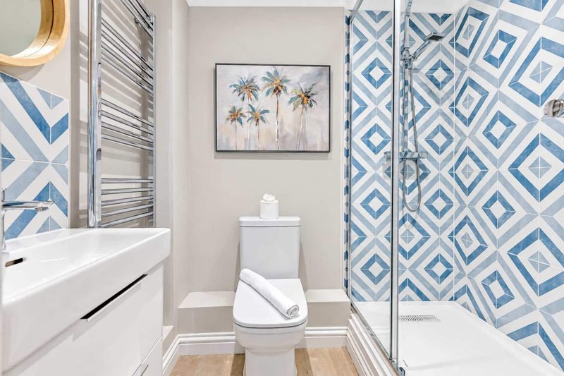 Modern bathroom with white vanity, toilet, shower enclosure and blue geometric tile pattern