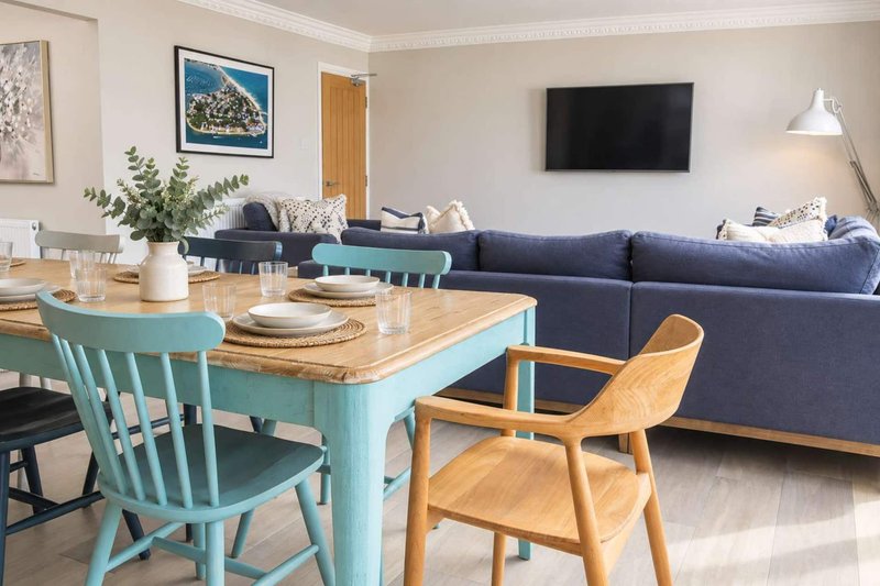 Open-plan living and dining area with turquoise dining table, wooden chairs, and navy sofa