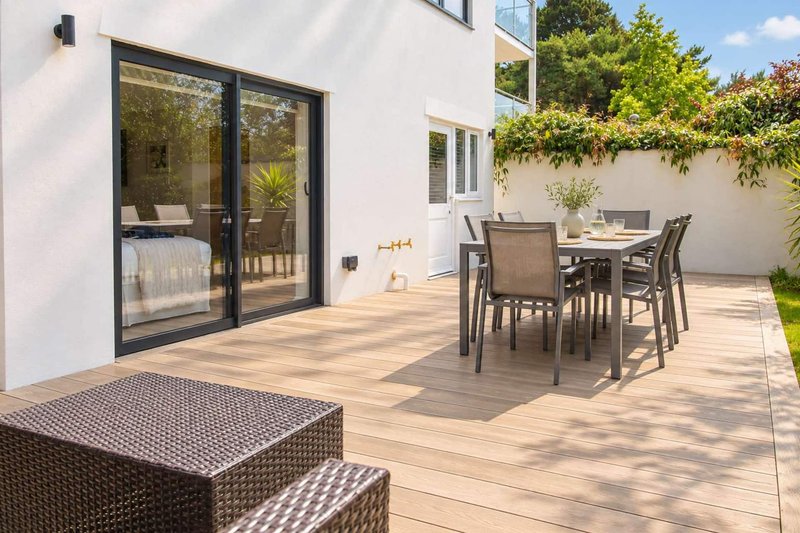 Modern patio with dining table, chairs, rattan seating and black-framed glass doors