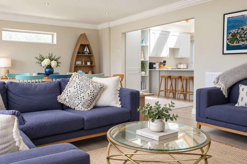 Open-plan living room with navy blue sofas, glass coffee table, and kitchen area visible through doorway