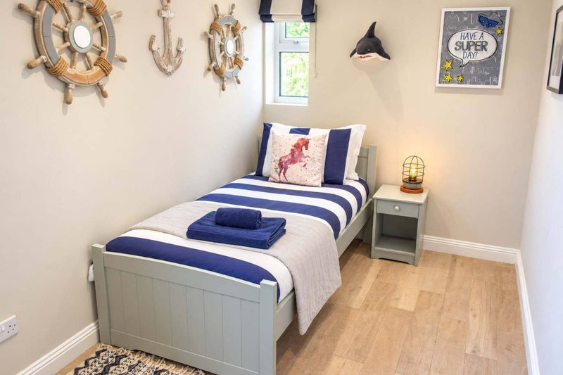 Bedroom with single bed, blue and white striped bedding, wooden floor and nautical wall decor
