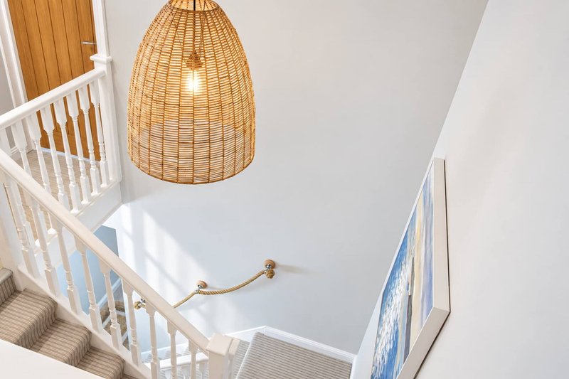 Staircase with white railing, woven pendant lamp, and wooden door visible from above