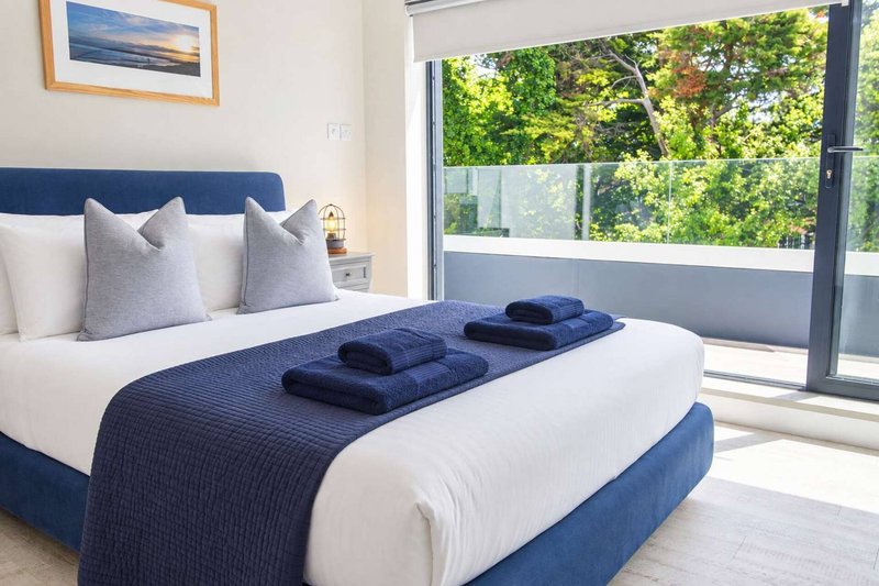Bright modern bedroom with blue upholstered bed, white bedding, and garden view through sliding doors