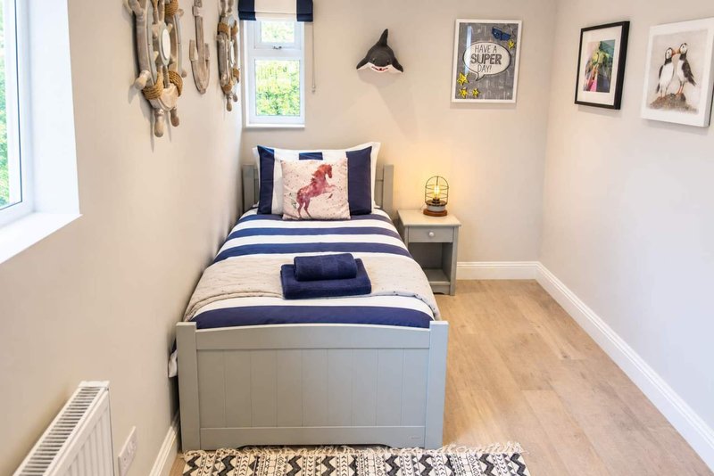 Small bedroom with single bed, navy striped bedding, wooden floor and framed wall art