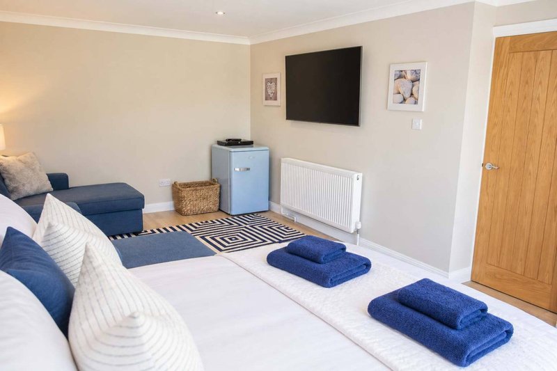 Bright bedroom with double bed, blue towels, TV mounted on wall, wooden door