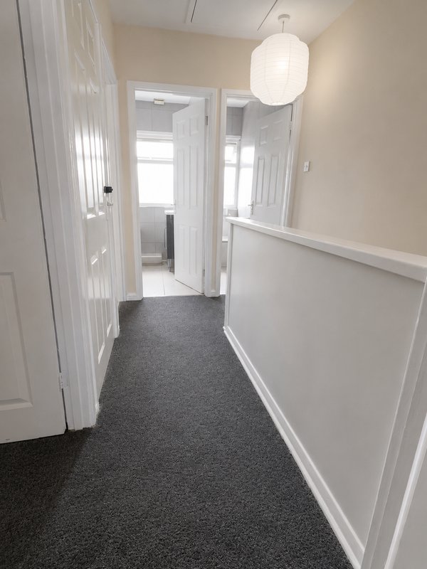 Bright hallway with white doors, gray carpet, pendant light and wainscoting